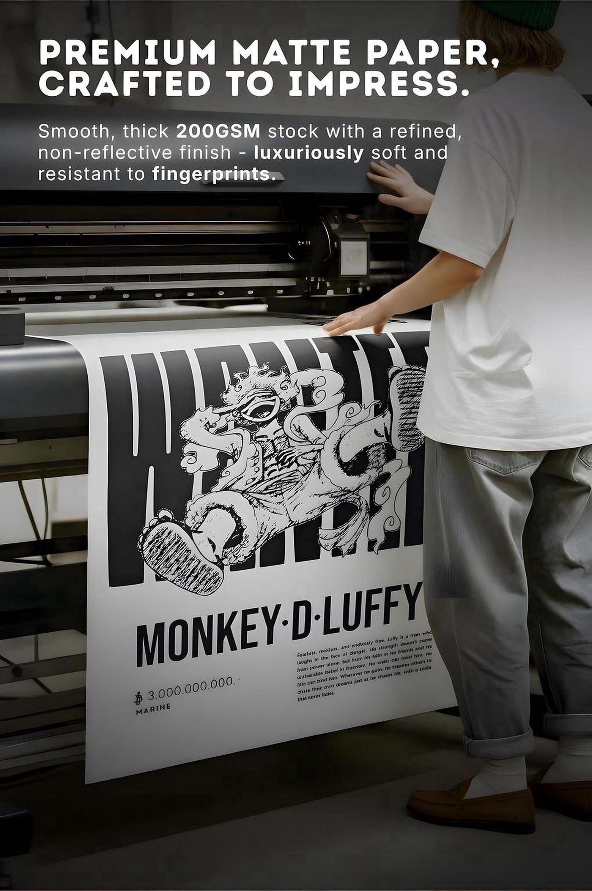 a person operating a printing press, with a large poster or banner prominently displayed in the foreground. The poster has a striking black and white design with a monkey-like figure, and the text on the poster reads "MONKEY-D-LUFFY".