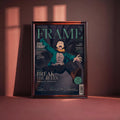 a framed magazine cover with an illustration of a person in a green jacket and black pants, appearing to be in a fighting stance. The cover has a dark background with text and graphics, and the magazine title "FRAME" is prominently displayed.